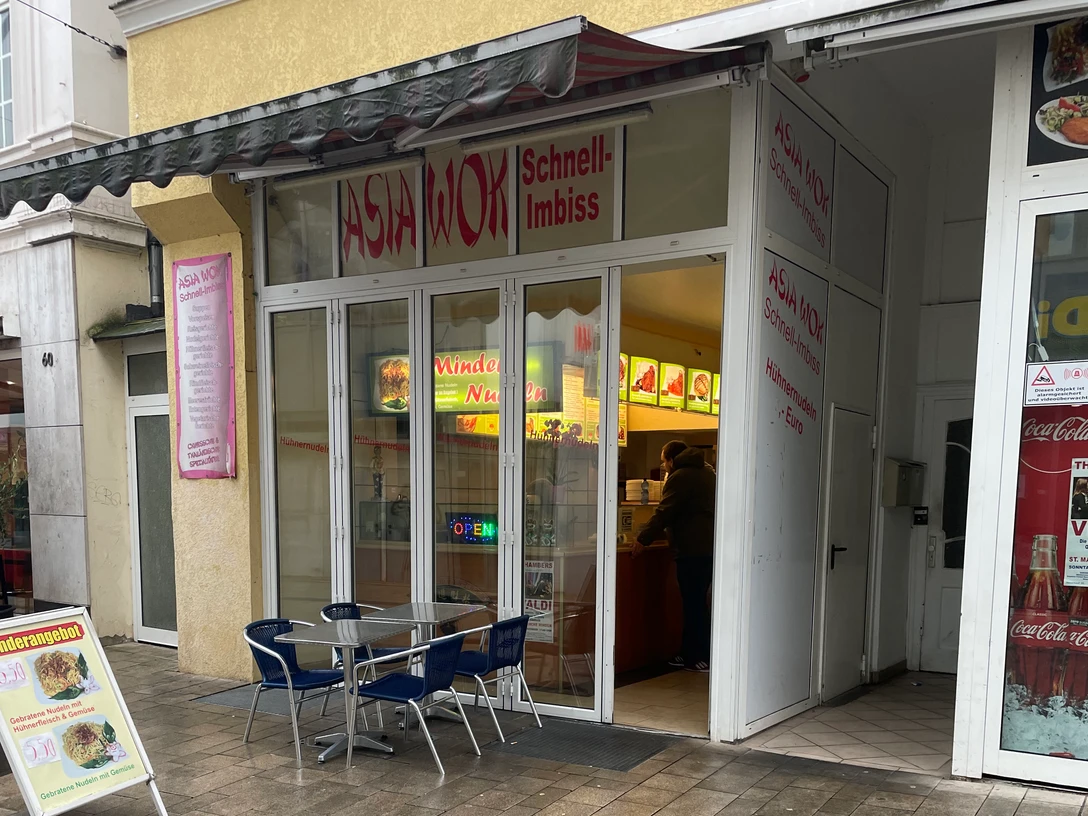 Asia Wok.jpg Das Bild zeigt einen Asia Wok Schnell-Imbiss mit Glasfronten und einem Tisch mit Stühlen davor.