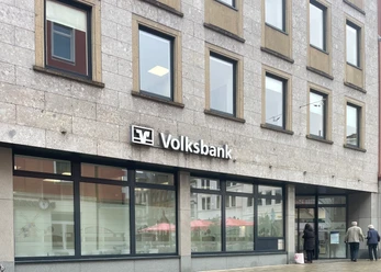 Voksbank.jpg Eine Volksbank mit großem Logo auf grauer Fassade, großen Fenstern und Passanten davor.
