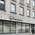 Voksbank.jpg Eine Volksbank mit großem Logo auf grauer Fassade, großen Fenstern und Passanten davor.