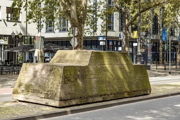 Motionless traffic A moss-covered concrete block with trees on it stands in the middle of an urban street scene.