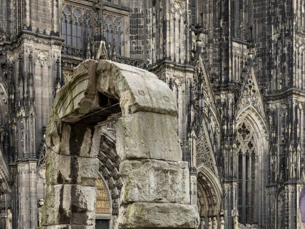 Römertorbogen Ein imposanter römischer Torbogen aus massiven Steinen, im Hintergrund die Fassade des Kölner Doms.