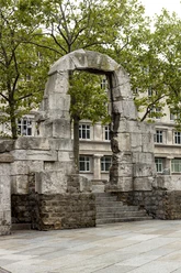 Römertorbogen Restaurierter Torbogen aus der römischen Antike in Köln, umrahmt von Bäumen, vor modernem Gebäude.