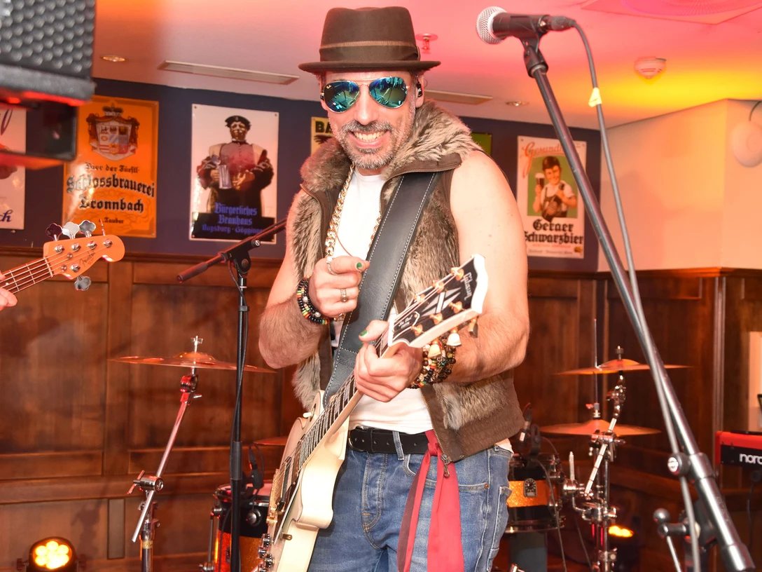 Cristobal.jpg Musiker trägt Sonnenbrille und Hut, spielt Gitarre mit Energie auf einer Bühne in einer Innenraumkneipe.