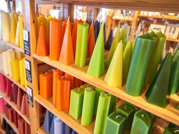Planken met kleurrijke kaarsen in verschillende vormen en kleuren, waaronder geel, oranje, groen en rood, in een gezellige winkel.