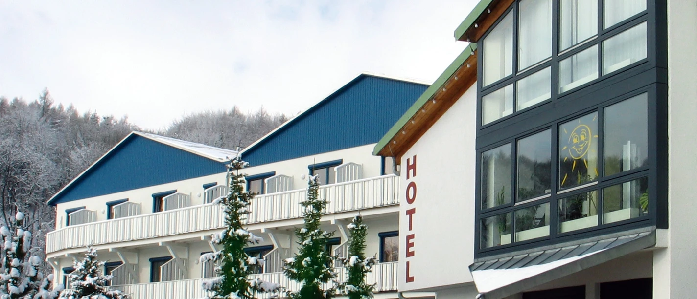 Hotel building in winter, with snow-covered trees and blue roof; clear, cold atmosphere.