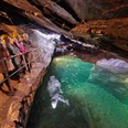 Führung im Besucherbergwerk "Marie Louise Stolln" Vier Personen mit gelben Helmen stehen auf einem Geländer in einer beleuchteten Höhle mit grünem Wasser, die Atmosphäre ist abenteuerlich.Four people in yellow helmets stand on a railing in an illuminated cave with green water, the atmosphere is adventurous.Čtyři lidé ve žlutých přilbách stojí na zábradlí v osvětlené jeskyni se zelenou vodou, atmosféra je dobrodružná.Cztery osoby w żółtych kaskach stoją na poręczy w oświetlonej jaskini z zieloną wodą, atmosfera jest pełna przygód.Vier mensen met gele helmen staan op een reling in een verlichte grot met groen water, de sfeer is avontuurlijk.Quattro persone con caschi gialli si trovano su una ringhiera in una grotta illuminata con acqua verde, l'atmosfera è avventurosa.