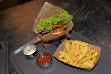 Burgermenü im WIDU Burger mit Salat, Tomaten und Zwiebeln, serviert mit Pommes frites, Sauce und Ketchup auf Tablett.