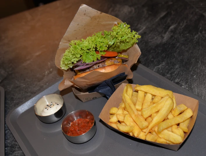 Burgermenü im WIDU Burger mit Salat, Tomaten und Zwiebeln, serviert mit Pommes frites, Sauce und Ketchup auf Tablett.