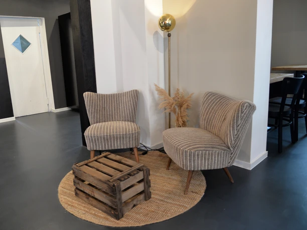 Zwei gepolsterte Sessel und ein kleiner Holztisch auf einem runden Teppich in einer modernen Raumecke.