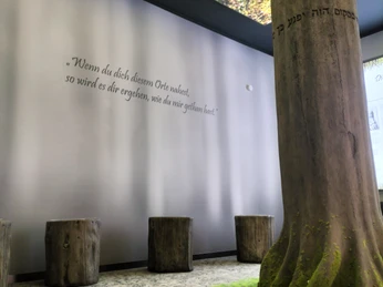 Ein Innenraum mit Baumstämmen als Sitzgelegenheiten und einer Säule, umgeben von Naturmotiven.