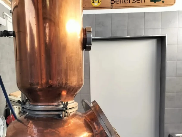 Kupferne Destillieranlage in einer Edelobstbrennerei mit Holzschild und glänzenden Armaturen.