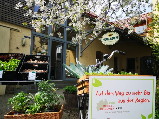 Willebadessen Hofladen Engemann Vor einem Holzgebäude voller Pflanzenkorb steht ein Fahrrad mit einem Schild über regionale Bio-Produkte.