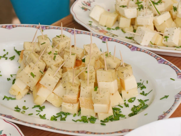 Borgentreich Körbecke Biohof Jacobi Würfel aus Käse mit Kräutern und Zahnstochern, angerichtet auf einem Teller mit feiner Verzierung.