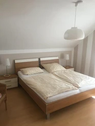 Schlafzimmer FeWo Brüggemann Helles Schlafzimmer mit modernem Doppelbett, Nachttischen aus Holz und sanfter Beleuchtung.