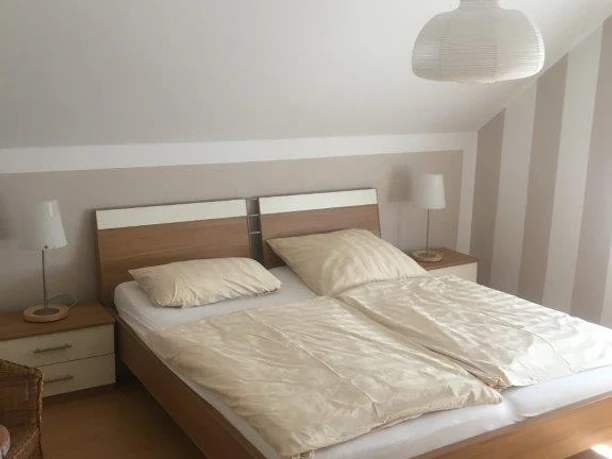Schlafzimmer FeWo Brüggemann Helles Schlafzimmer mit modernem Doppelbett, Nachttischen aus Holz und sanfter Beleuchtung.