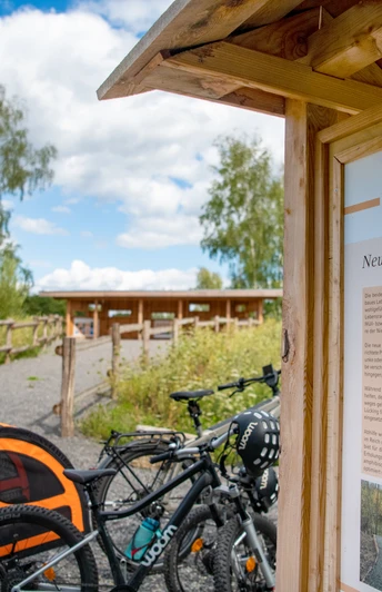 Fahrräder und ein Hundewagen vor einer Info-Tafel in einer landschaftlichen Naturanlage.