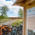 Neustart in der Tongrube.jpg Fahrräder und ein Hundewagen vor einer Info-Tafel in einer landschaftlichen Naturanlage.