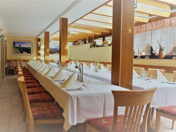 Hotel Elbpromenade Tafel Mittag Langer, festlich gedeckter Tisch in einem hellen Raum mit Holzsäulen, weißen Tischdecken, gefalteten Servietten und Blumenarrangement.