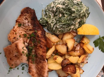 Lachs Gegrilltes Lachsfilet mit knusprigen Kartoffeln, cremigem Spinat und Zitronenspalte auf Teller.