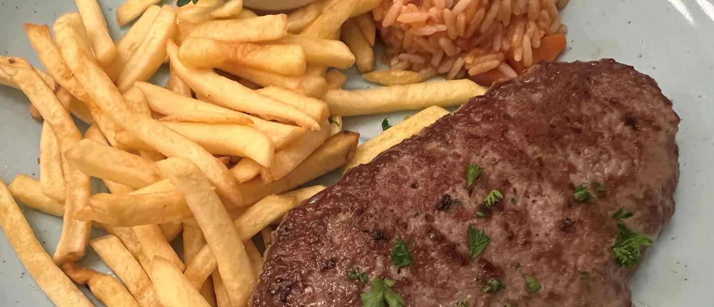 A juicy minced steak with parsley garnish, French fries and tomato rice on a blue ceramic plate.