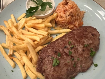 Hacksteak Ein saftiges Hacksteak mit Petersiliengarnitur, Pommes frites und Tomatenreis auf blauer Keramikplatte.