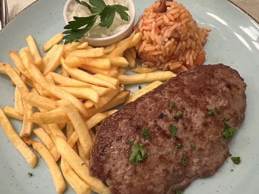 Hacksteak Ein saftiges Hacksteak mit Petersiliengarnitur, Pommes frites und Tomatenreis auf blauer Keramikplatte.