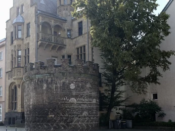 Römerturm Auf dem Bild ist der historische Römerturm in Köln zu sehen, ein gut erhaltenes Stadttor von ehemals 19 Türmen der römischen Stadtmauer, im Hintergrund das gotische Gebäude mit markanten Verzierungen und Erker, flankiert von einem üppigen Baum.The picture shows the historic Römerturm in Cologne, a well-preserved city gate of the former 19 towers of the Roman city wall, in the background the Gothic building with striking decorations and bay windows, flanked by a lush tree.