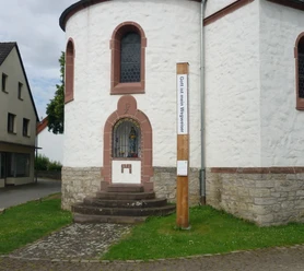 Bibel-Pfahl in Hembsen Runder Kirchturm mit steinernen Stufen, bunt verglastes Fenster, daneben ein hölzerner Bibel-Pfahl.