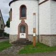 Bibel-Pfahl in Hembsen Runder Kirchturm mit steinernen Stufen, bunt verglastes Fenster, daneben ein hölzerner Bibel-Pfahl.