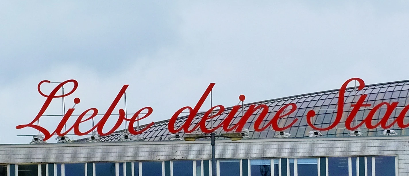 LiebedeineStadt Building with red lettering “'Liebe deine Stadt”' on the roof, cloudy sky in the background.