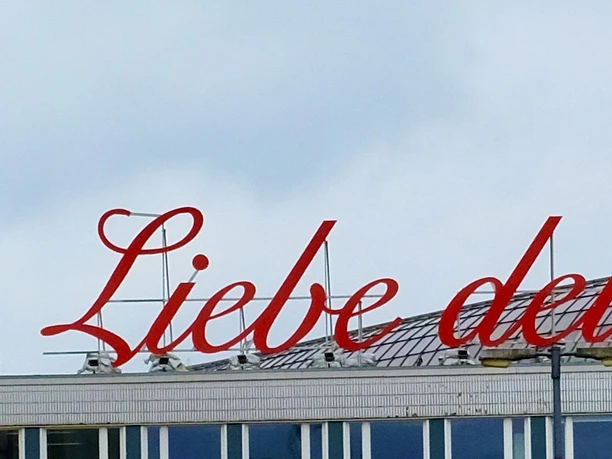 LiebedeineStadt Building with red lettering “'Liebe deine Stadt”' on the roof, cloudy sky in the background.