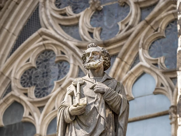 St. Peter's Fountain A statue of St. Peter, wrapped in a long robe, stands elevated in front of Gothic windows.
