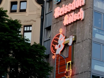 Reissdorf neon sign Neonreklame „Trinkt Reissdorf Kölsch“ mit lächelnder Figur an einer Gebäudeaußenwand in Köln.Neon sign "Trinkt Reissdorf Kölsch" with a smiling figure on the outside wall of a building in Cologne.