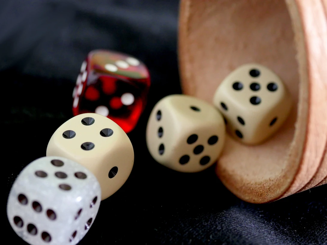 Verknobelung.jpg Vier Würfel, drei weiße und ein roter, liegen neben einem umgekippten Becher auf schwarzem Stoff.
