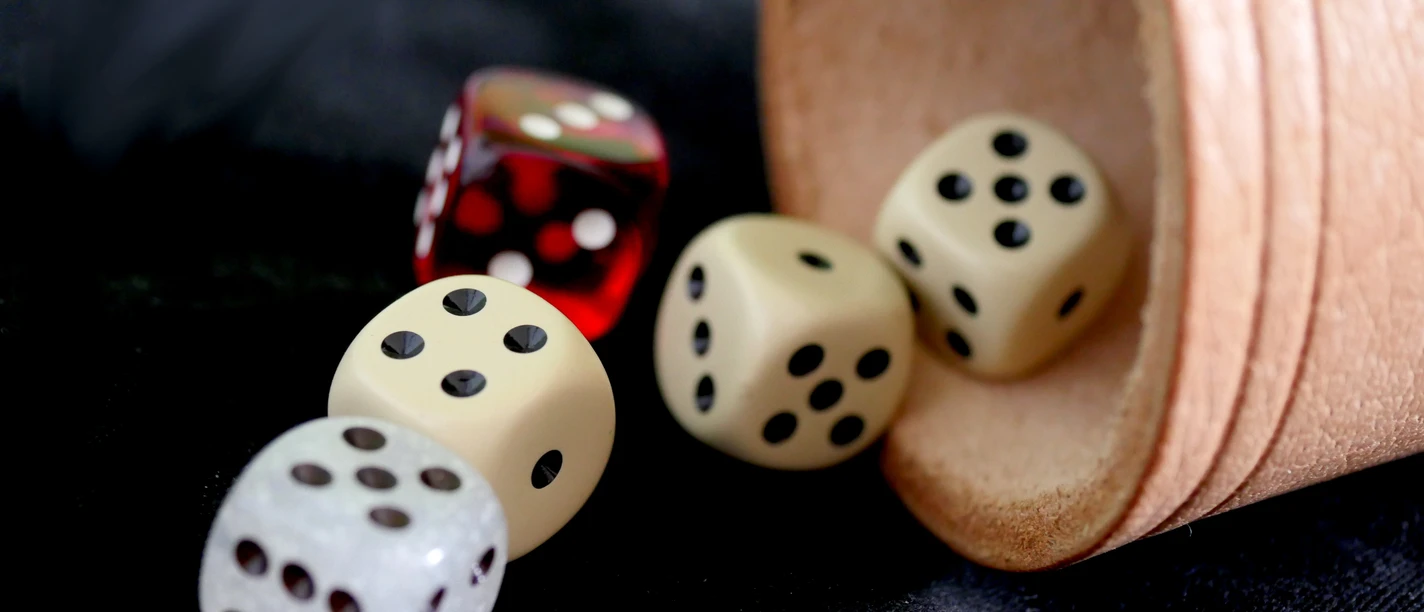 Verknobelung.jpg Vier Würfel, drei weiße und ein roter, liegen neben einem umgekippten Becher auf schwarzem Stoff.