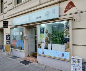 Kiosk Hanoi Die Fassade ist mit großen Fenstern ausgestattet, hinter denen Dekorationen und Pflanzen zu sehen sind. Ein Schild mit dem Namen des Geschäfts und Informationen über das angebotene Sortiment befindet sich oberhalb der Fenster. Vor dem Kiosk steht ein Aufsteller mit weiteren Details zu den angebotenen Produkten. Die Fenster sind mit Illustrationen von Bubble Tea verziert.