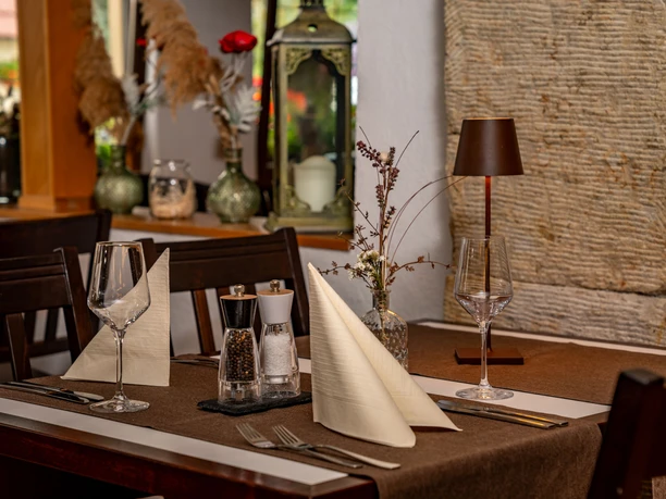 Elegante restauranttafel met bruin tafelkleed, twee wijnglazen, gevouwen servetten, peper- en zoutstel en een kleine tafellamp.