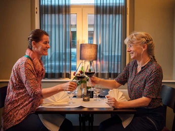 Logis Hotel Quartier 5 Zwei Frauen sitzen an einem Tisch in einem Restaurant und stoßen mit Rotweingläsern an, lächelnd und in entspannter Atmosphäre.Two women sit at a table in a restaurant and toast with glasses of red wine, smiling and in a relaxed atmosphere.Dvě ženy sedí u stolu v restauraci a připíjejí si sklenkami červeného vína, usmívají se a jsou v uvolněné atmosféře.Dwie kobiety siedzą przy stoliku w restauracji i wznoszą toast kieliszkami czerwonego wina, uśmiechnięte i w swobodnej atmosferze.Twee vrouwen zitten aan een tafel in een restaurant en toosten met glazen rode wijn, glimlachend en in een ontspannen sfeer.Due donne siedono al tavolo di un ristorante e brindano con bicchieri di vino rosso, sorridendo e in un'atmosfera rilassata.