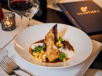 Ein elegantes Gericht mit Fleisch, Schaum und Gemüse auf weißem Teller, umgeben von Weingläsern und einer Kerze auf einem gedeckten Tisch.An elegant dish with meat, foam and vegetables on a white plate, surrounded by wine glasses and a candle on a laid table.Elegantní pokrm s masem, pěnou a zeleninou na bílém talíři, obklopený skleničkami na víno a svíčkou na prostřeném stole.Eleganckie danie z mięsem, pianką i warzywami na białym talerzu, otoczone kieliszkami do wina i świecą na nakrytym stole.Een elegant gerecht met vlees, schuim en groenten op een wit bord, omringd door wijnglazen en een kaars op een gedekte tafel.Un piatto elegante con carne, spuma e verdure su un piatto bianco, circondato da bicchieri di vino e una candela su una tavola imbandita.