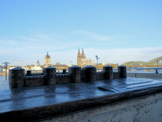Kastell Divitia-Deutz Bronzemodell des römischen Kastells Divitia vor der Kulisse des Kölner Doms und der Hohenzollernbrücke am Rheinufer. Der Himmel ist klar und blau.A miniature model of Kastell Divitia with Cologne Cathedral and Hohenzollern Bridge in the background.