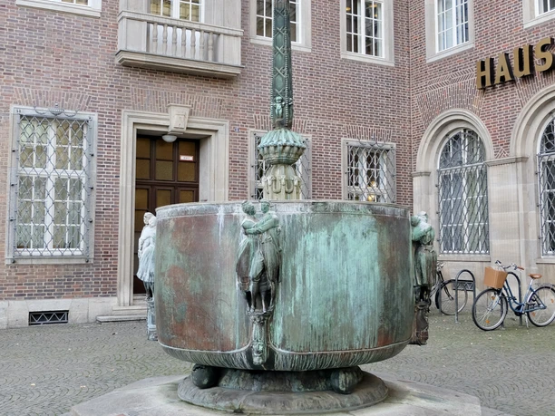 Fastnachtsbrunnen Fastnachtsbrunnen vor dem historischen Gebäude in Köln, mit bogenförmigen Figuren und Brunnenbecken.