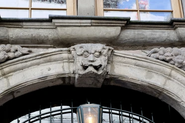 Grinkopf Steinerner Grinkopf mit kunstvoller Fratze über einem Bogen, eingerahmt von Fruchtmotiven.