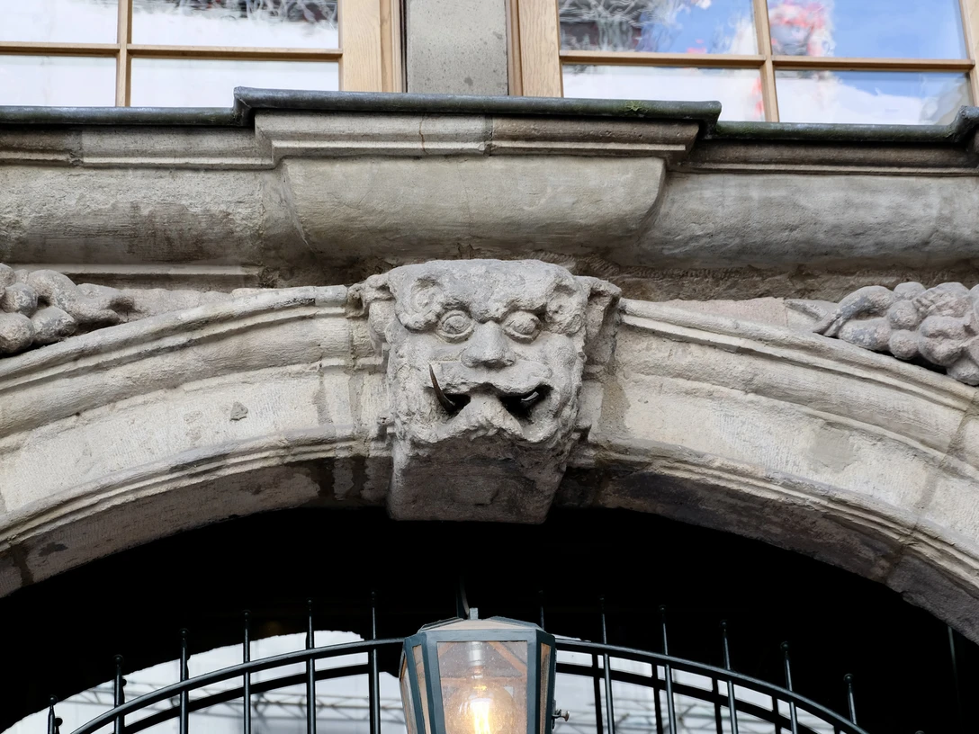 Grinkopf Steinerner Grinkopf mit kunstvoller Fratze über einem Bogen, eingerahmt von Fruchtmotiven.Stone grin head with artistic grimace above an arch, framed by fruit motifs.