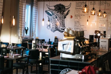 Mann und Metzger Wand Ein stilvolles Restaurant mit Holzdecken, Wandkunst eines Stieres und eleganter Beleuchtung.
