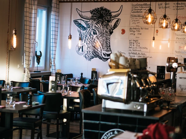 Mann und Metzger Wand Ein stilvolles Restaurant mit Holzdecken, Wandkunst eines Stieres und eleganter Beleuchtung.