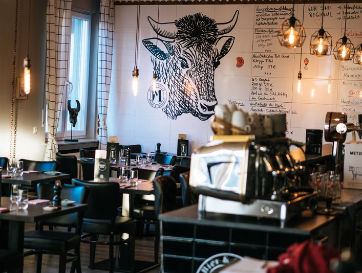 Mann und Metzger Wand Ein stilvolles Restaurant mit Holzdecken, Wandkunst eines Stieres und eleganter Beleuchtung.