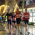 Christkindllauf Wiedenbrück Läufer in einem nächtlichen Stadtmarathon bei Regen, umgeben von festlich beleuchteten Fachwerkhäusern.