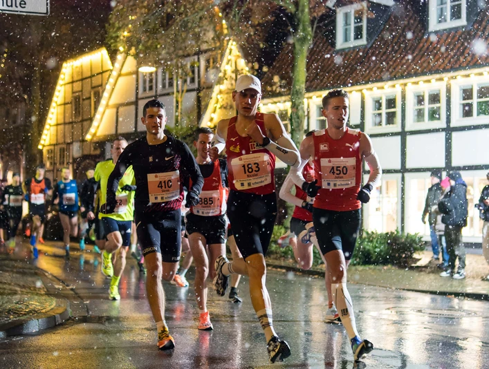 Christkindllauf Wiedenbrück Läufer in einem nächtlichen Stadtmarathon bei Regen, umgeben von festlich beleuchteten Fachwerkhäusern.