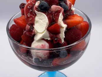 Eiscafé Smile Eisbecher Fruchtiges Dessert in einer blauen Glasschale mit Sahne, Erdbeeren, Himbeeren, Blaubeeren und roter Soße.