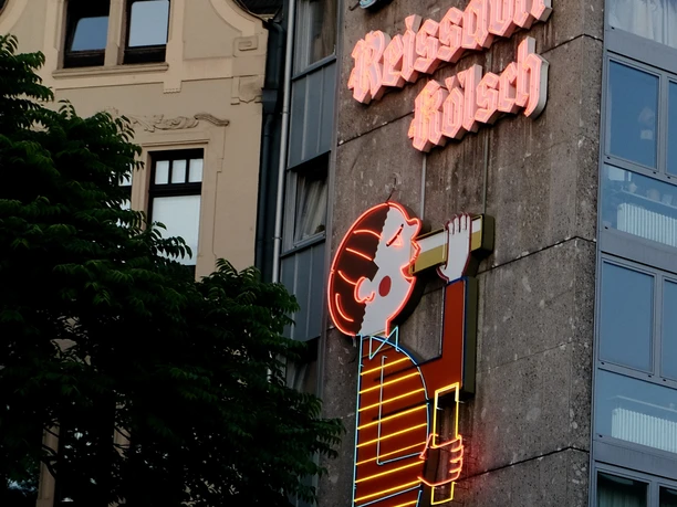 Reissdorf Leuchtreklame Neonreklame am Kölner Gebäude zeigt das ikonische Reissdorf-Kölsch-Logo, umgeben von Architektur.